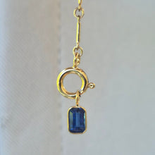 Load image into Gallery viewer, Gold necklace with a blue gemstone pendant held by a hand against a white background
